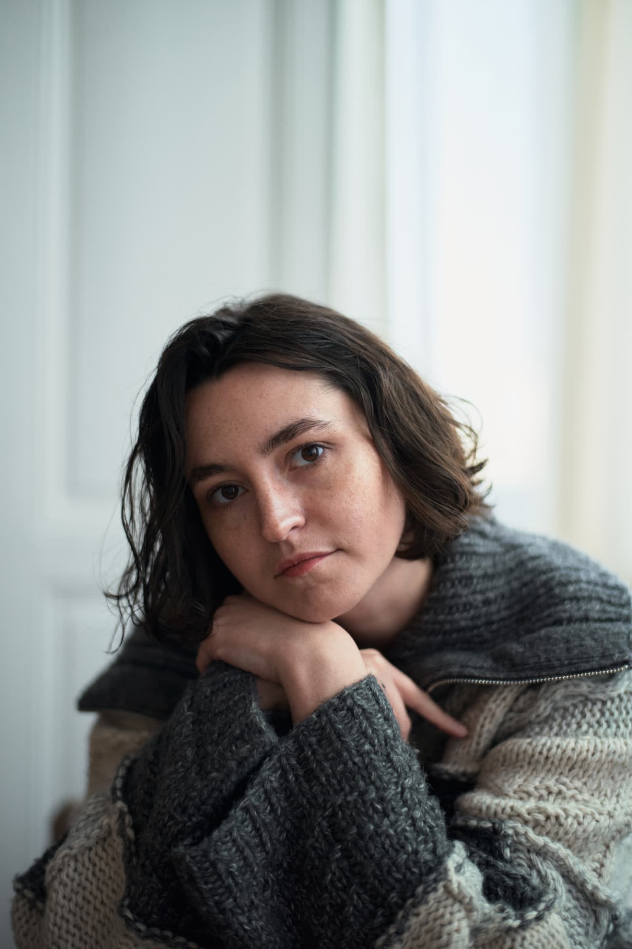Woman with short dark hair resting her chin on her hands, looking calmly at the camera
