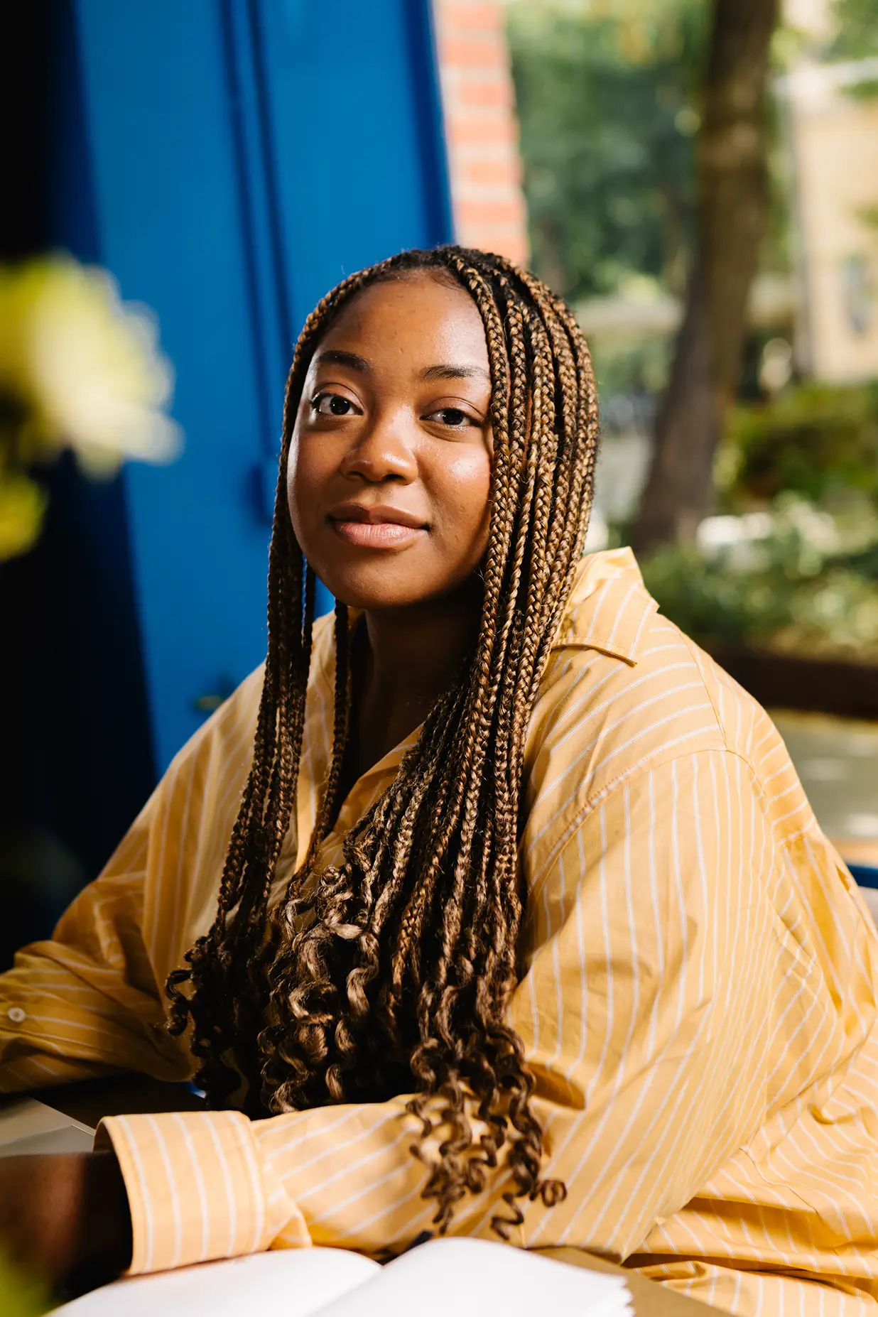 Woman with long braids in a yellow striped shirt smiling over an open book