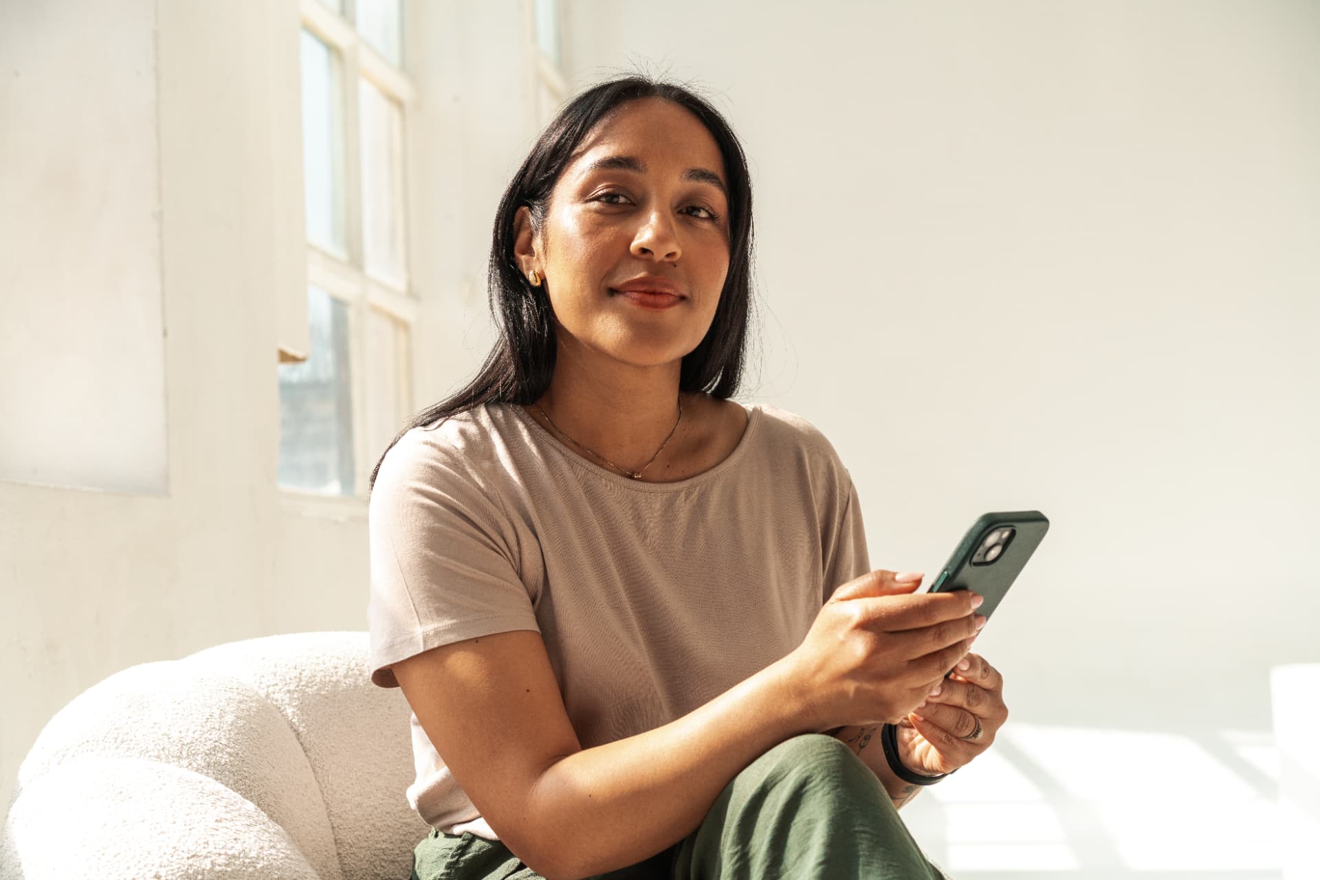 Woman with long dark hair holding her phone, smiling softly